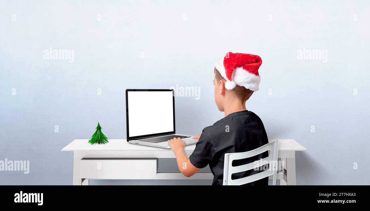 Boy in Christmas hat works on laptop with isolated screen. Mockup for greeting text od app, web page presentation.. Copy space for holiday creativity Stock Photo