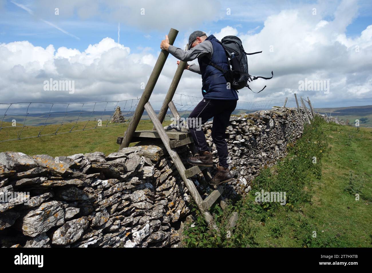 Elderly Man Climbing Wooden Ladder Stile over Dry Stone Wall to the Summit Cairn of Addlebrough in Wensleydale, Yorkshire Dales, England, UK. Stock Photo