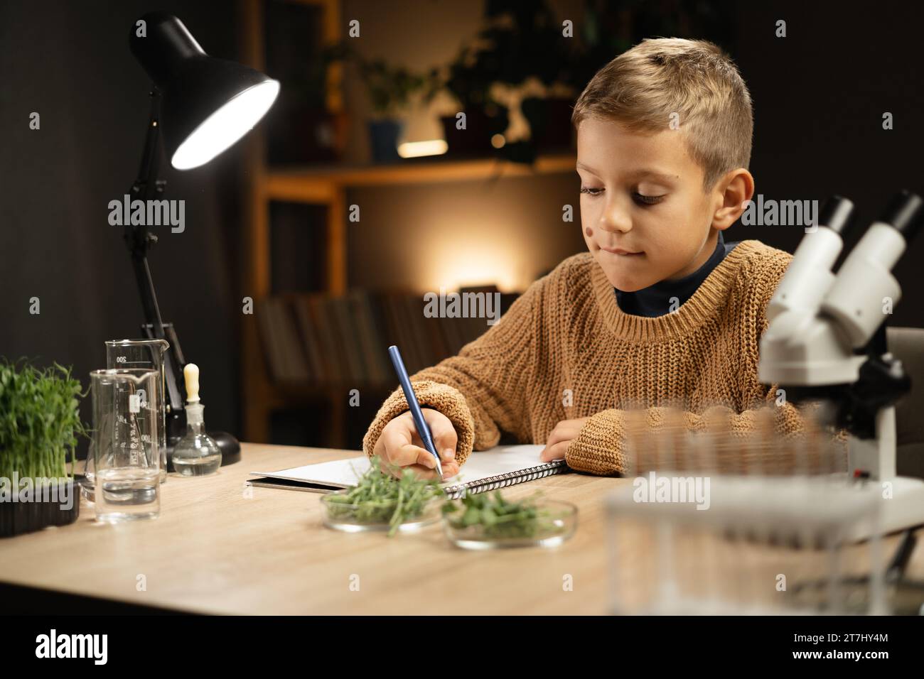 Smart boy student confident using microscope, making notes in notebook