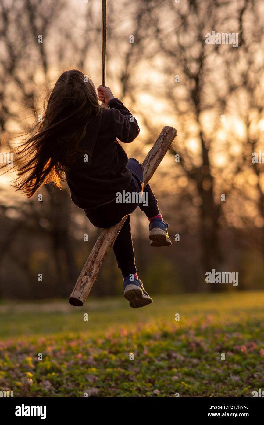 Unrecognizable little girl swings on homemade swing in nature, in park, in village, in children's camp. Outdoor games and entertainment. Happy childho Stock Photo