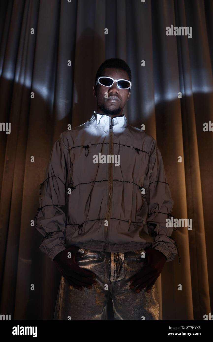 Dramatic fashion portrait of young Black man wearing sunglasses and looking at camera posing in silver outfit Stock Photo