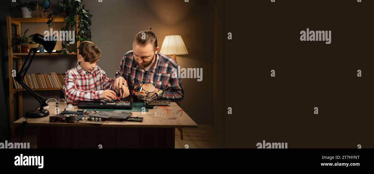 Dad and son wear and eyeglasses working with soldering iron while fixing broken details from laptop computer Stock Photo