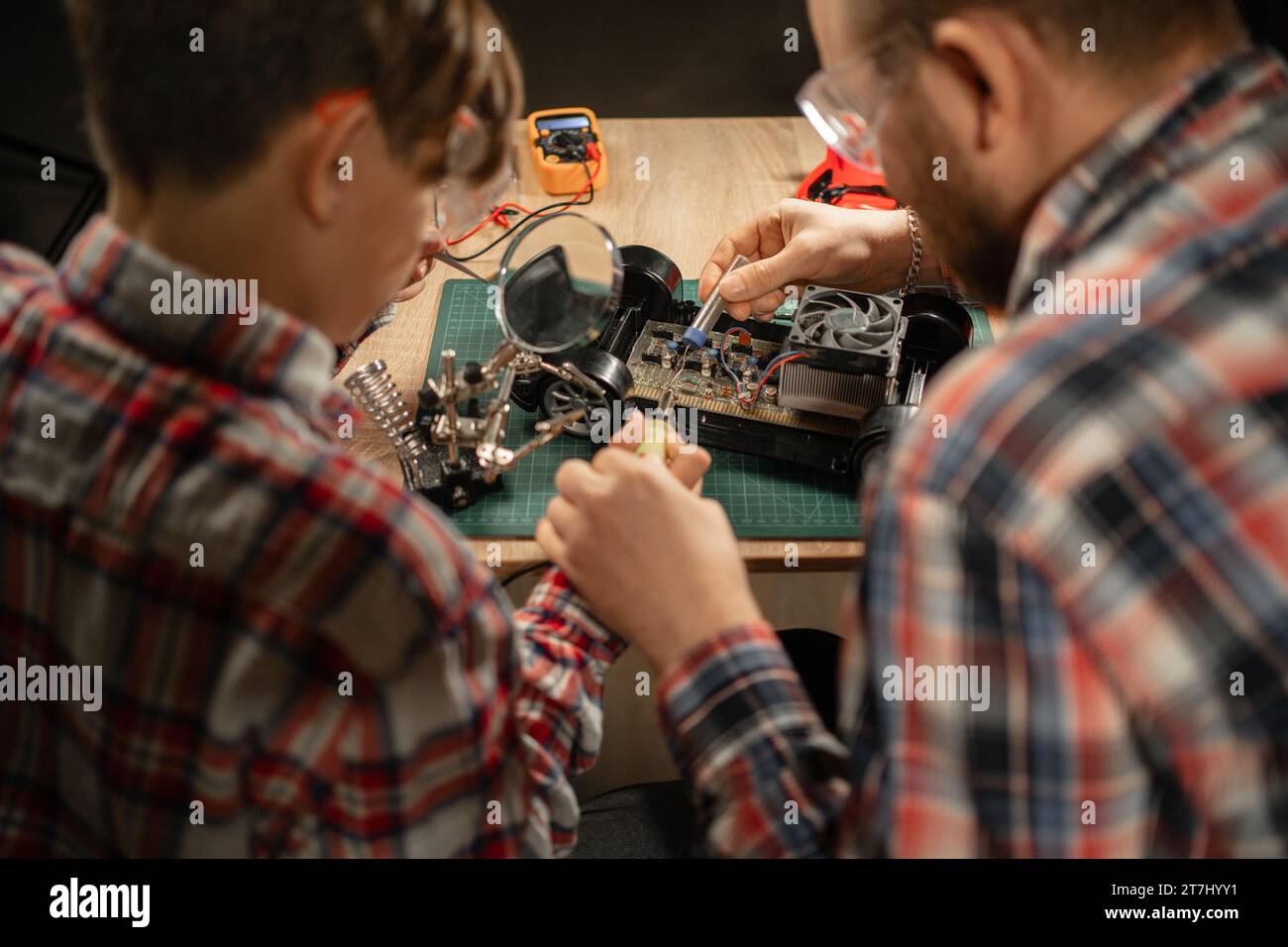 Father and son in safety glasses are soldering a broken machine on the