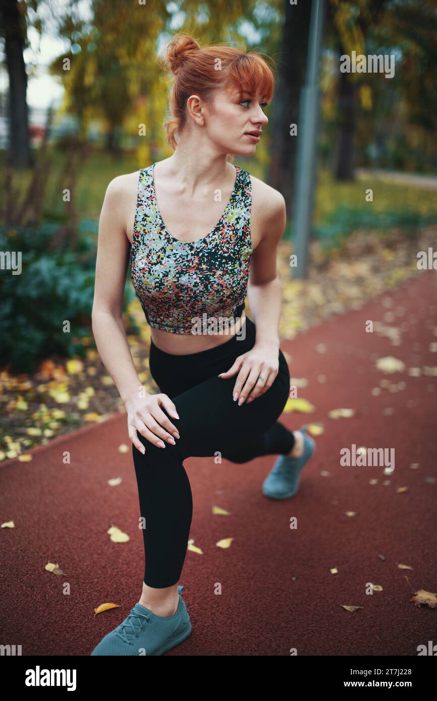 Young Caucasian redhead woman stretching before running in nature at autumn, looking away Stock Photo