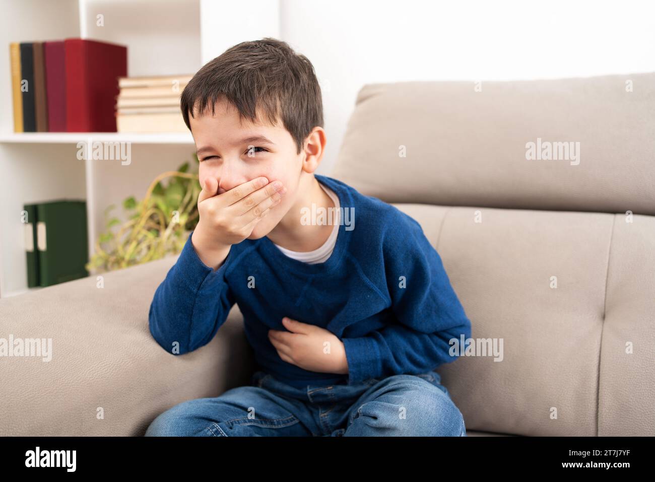 Stressed child with a stomach ache about to vomit on a couch at home