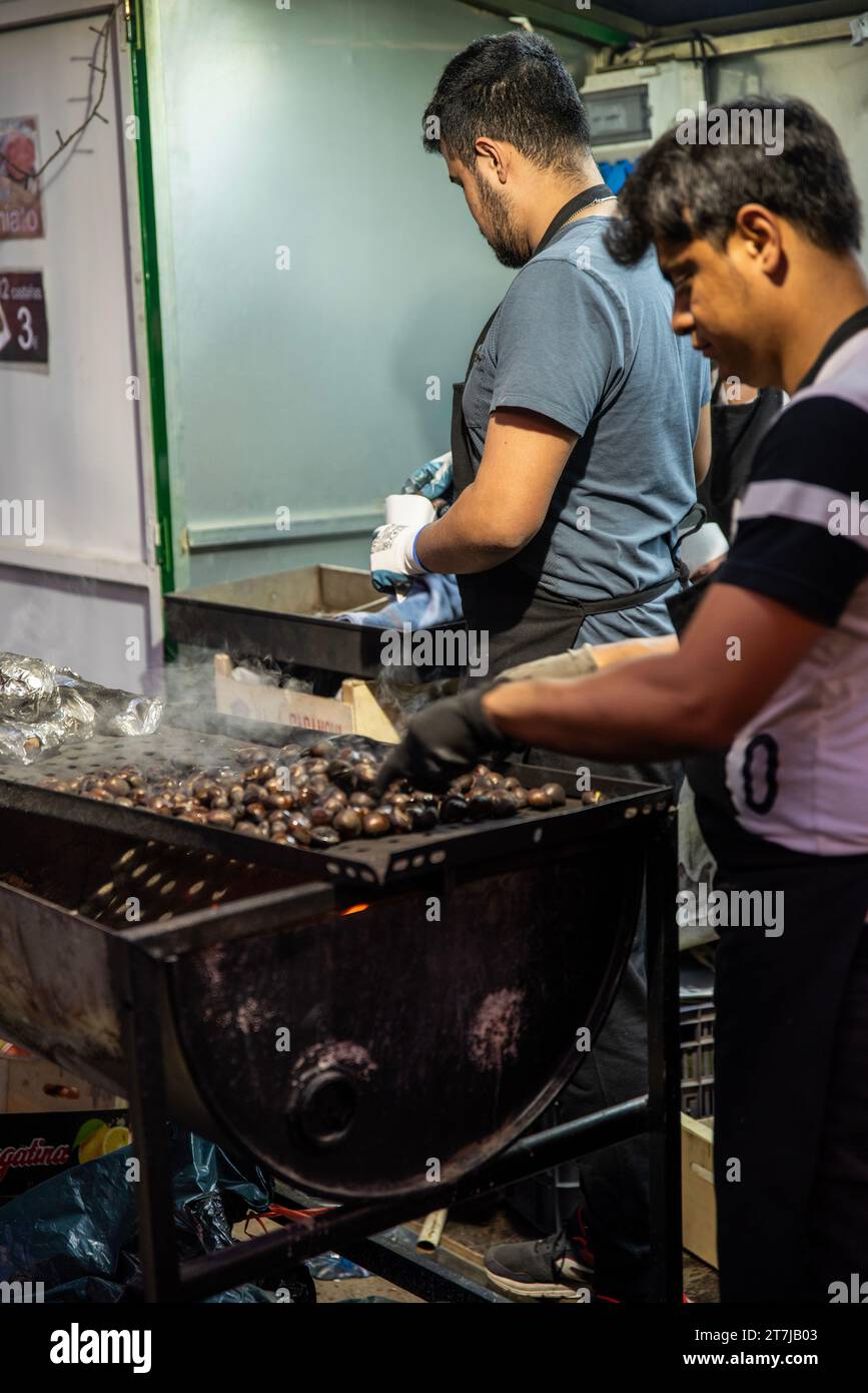 Capture the essence of tradition: Two men expertly roasting chestnuts at a cozy street stall, filling the air with the irresistible aroma of warm, sea Stock Photo