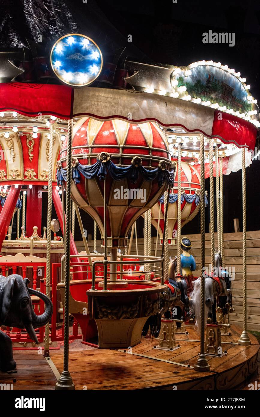 Bathed in rain-kissed nostalgia, a timeless wooden carousel adorned with golden and red lights illuminates the night, its whimsical balloons and charm Stock Photo