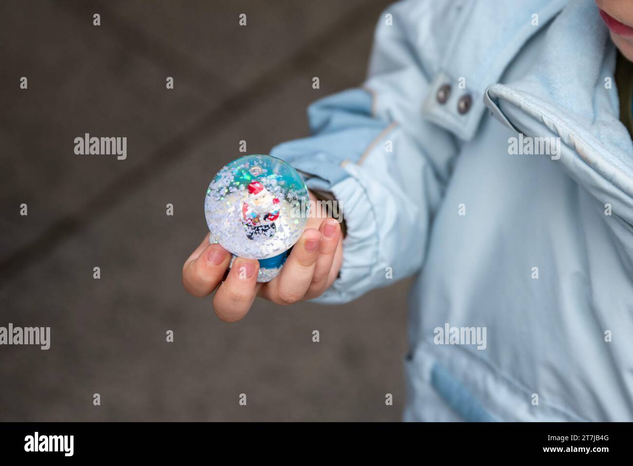 Childhood Wonder: Tiny hands cradle a Christmas snow globe, capturing the enchantment of Santa Claus amid swirling snow inside. Stock Photo