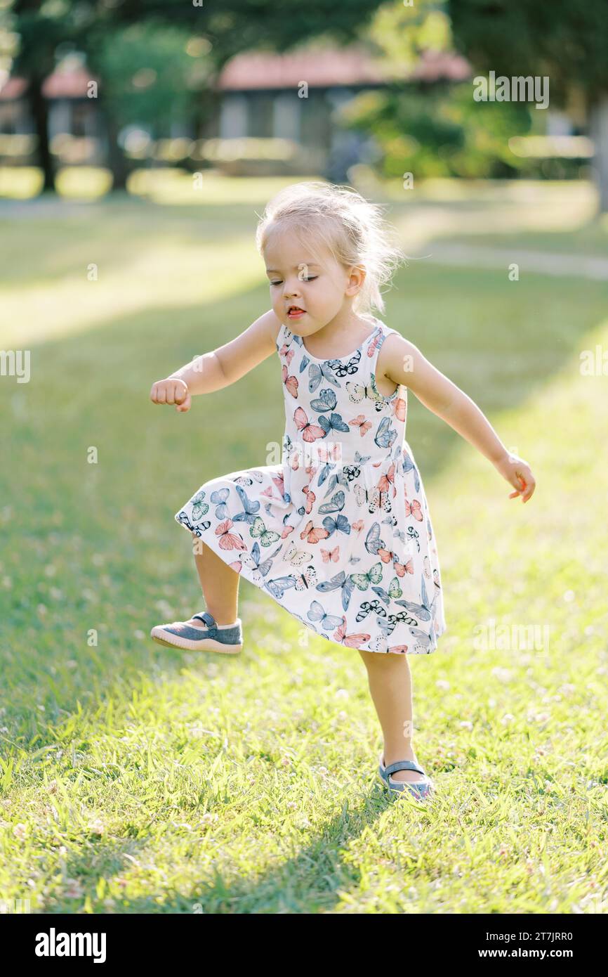 Little girl funny stamping her feet in a sunny meadow and waving her arms Stock Photo