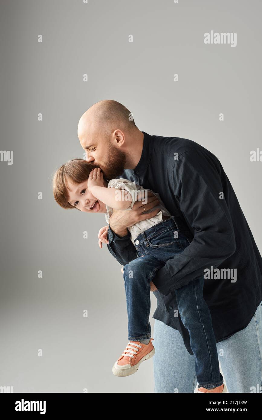 vertical shot of happy bearded father holding and kissing his playful jolly son, modern parenting Stock Photo