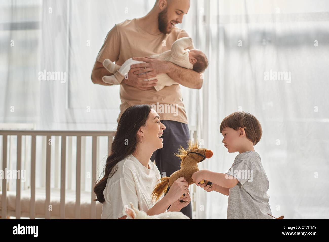 focus on mother playing with toy horse with her little son next to her blurred husband and baby boy Stock Photo