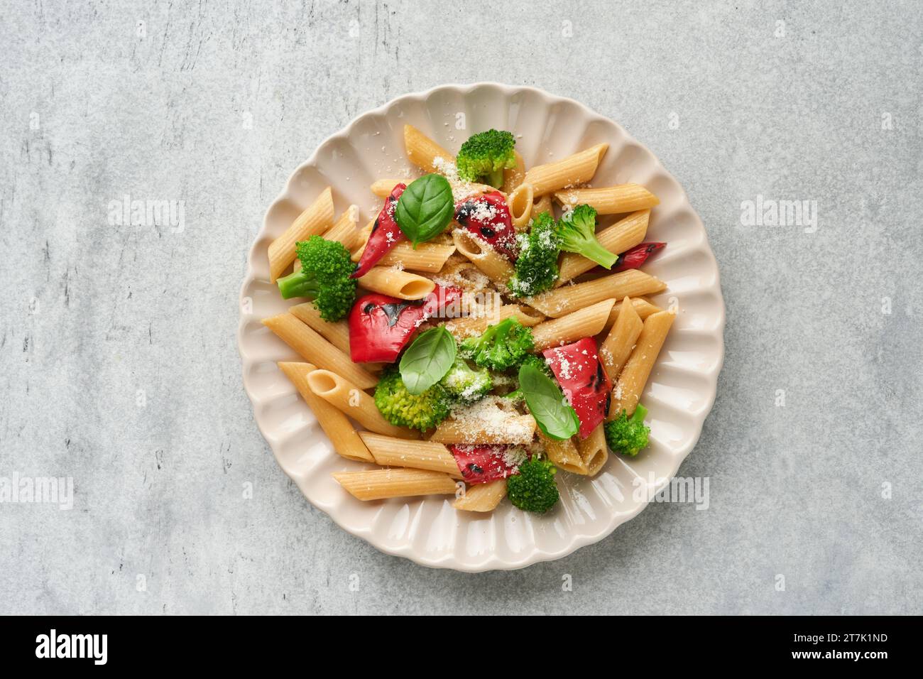 Wholegrain pasta penne with broccoli and red grilled bell pepper and on light grey slate, stone or concrete background. Vegan pasta. Traditional Itali Stock Photo