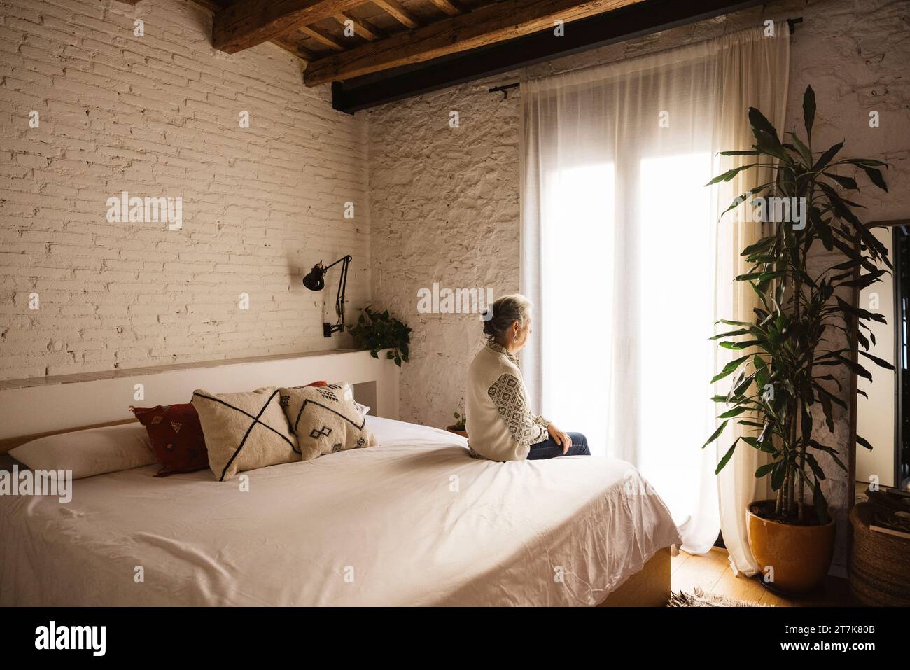 Portrait of thoughtful real mature senior woman sitting on bed in front