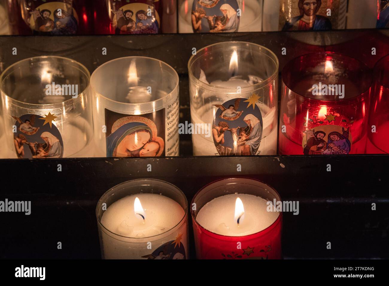 Selestat, France - December 25, 2022: Catholic prayer candles, with Holy Family and Mary with baby Jesus, glow in darkness in church in Christmas Eve. Stock Photo