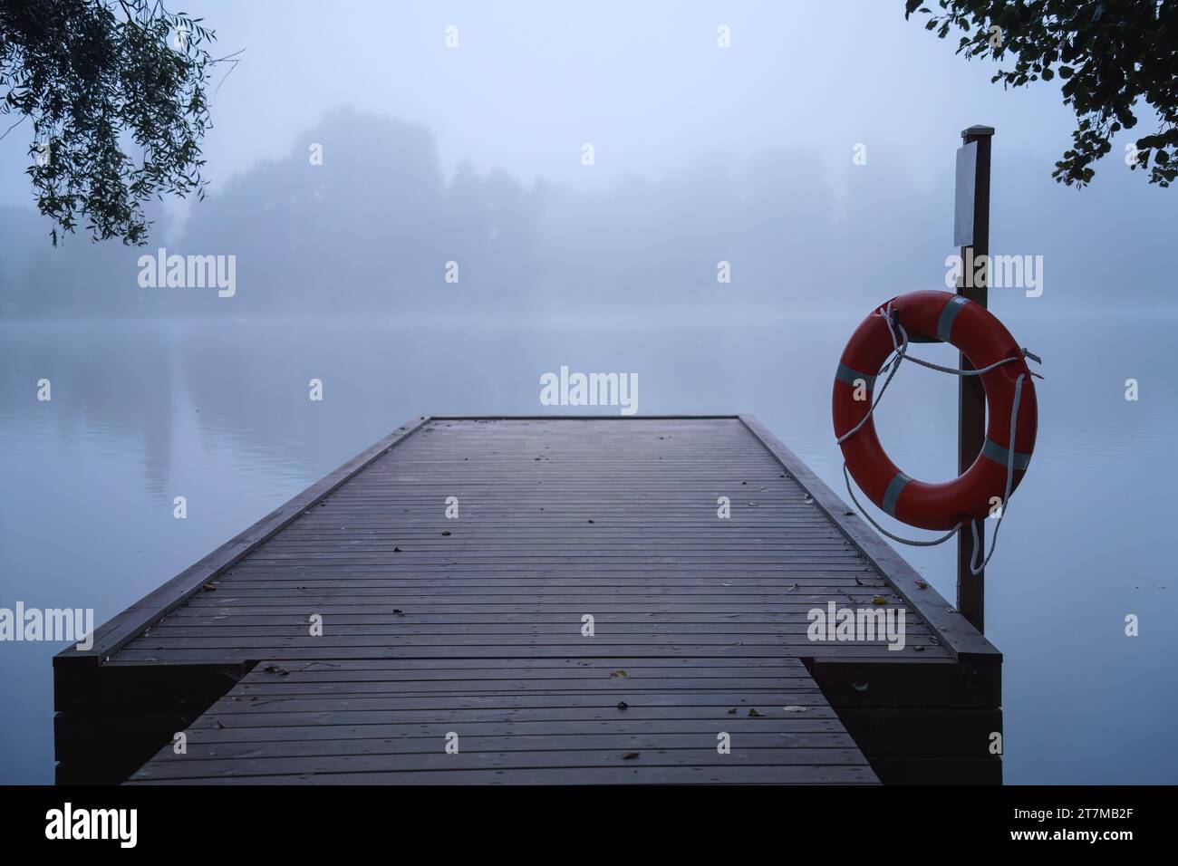 Wooden pier in the blue morning mist, with a life preserver ring hanging on a pole Stock Photo