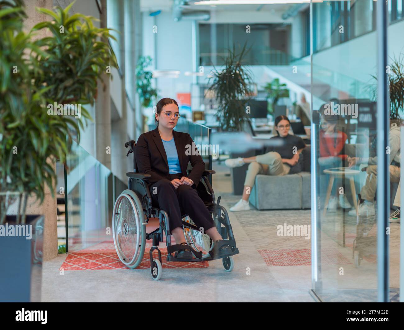 In a modern office, a young businesswoman in a wheelchair is surrounded ...