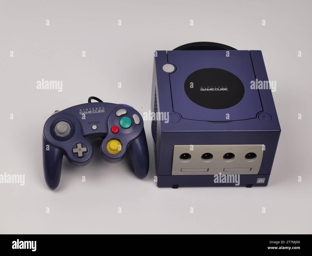 A Purple Nintendo GameCube console with a purple joypad on a white background. Stock Photo
