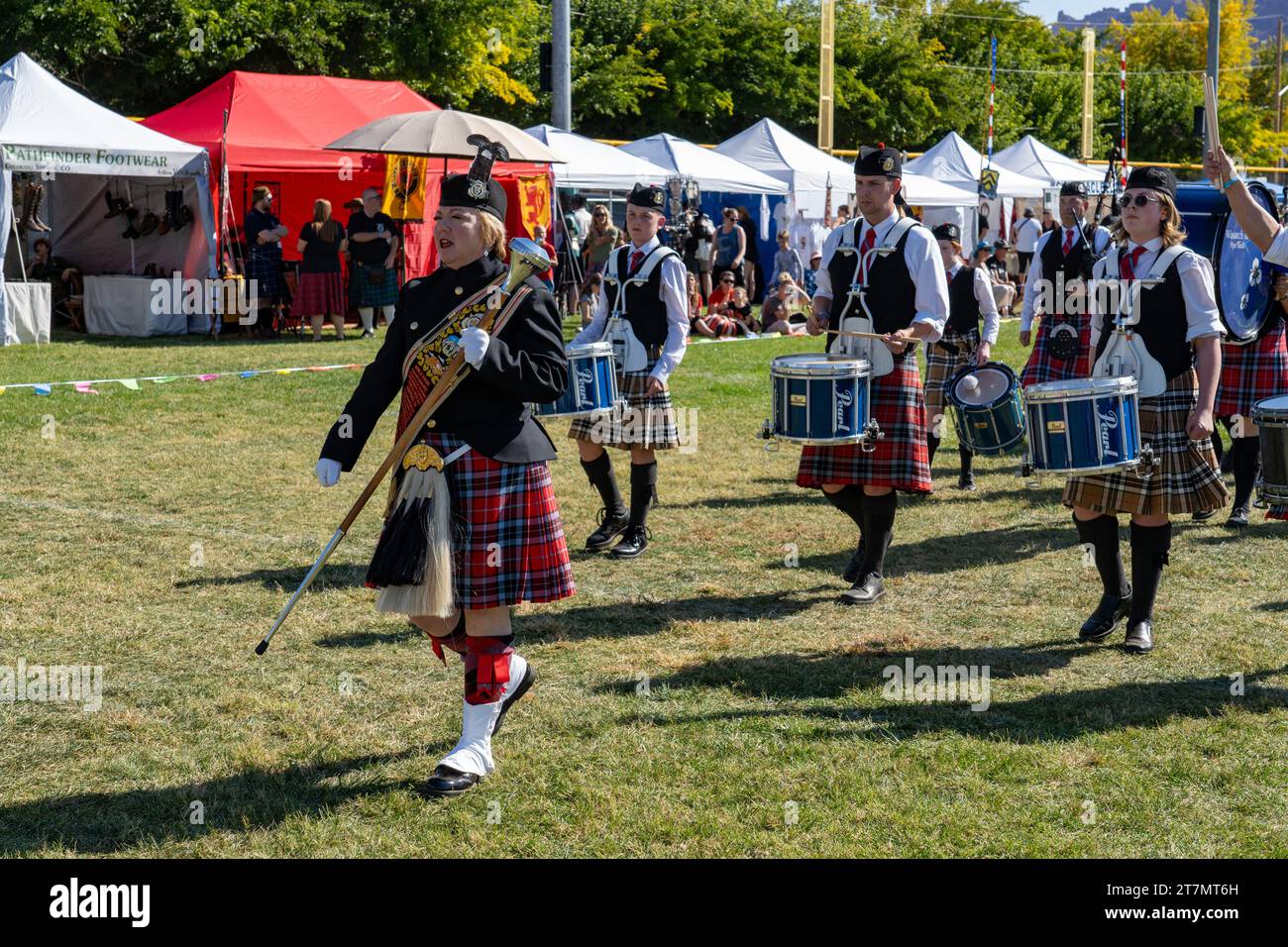 A female drum major in full regalia leads a Scottish pipe band at the