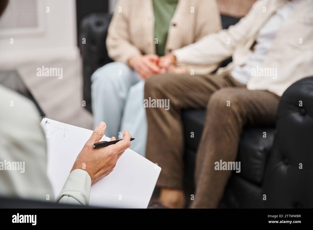 focus on psychologist  holding pen and blank notebook near married couple during appointment Stock Photo