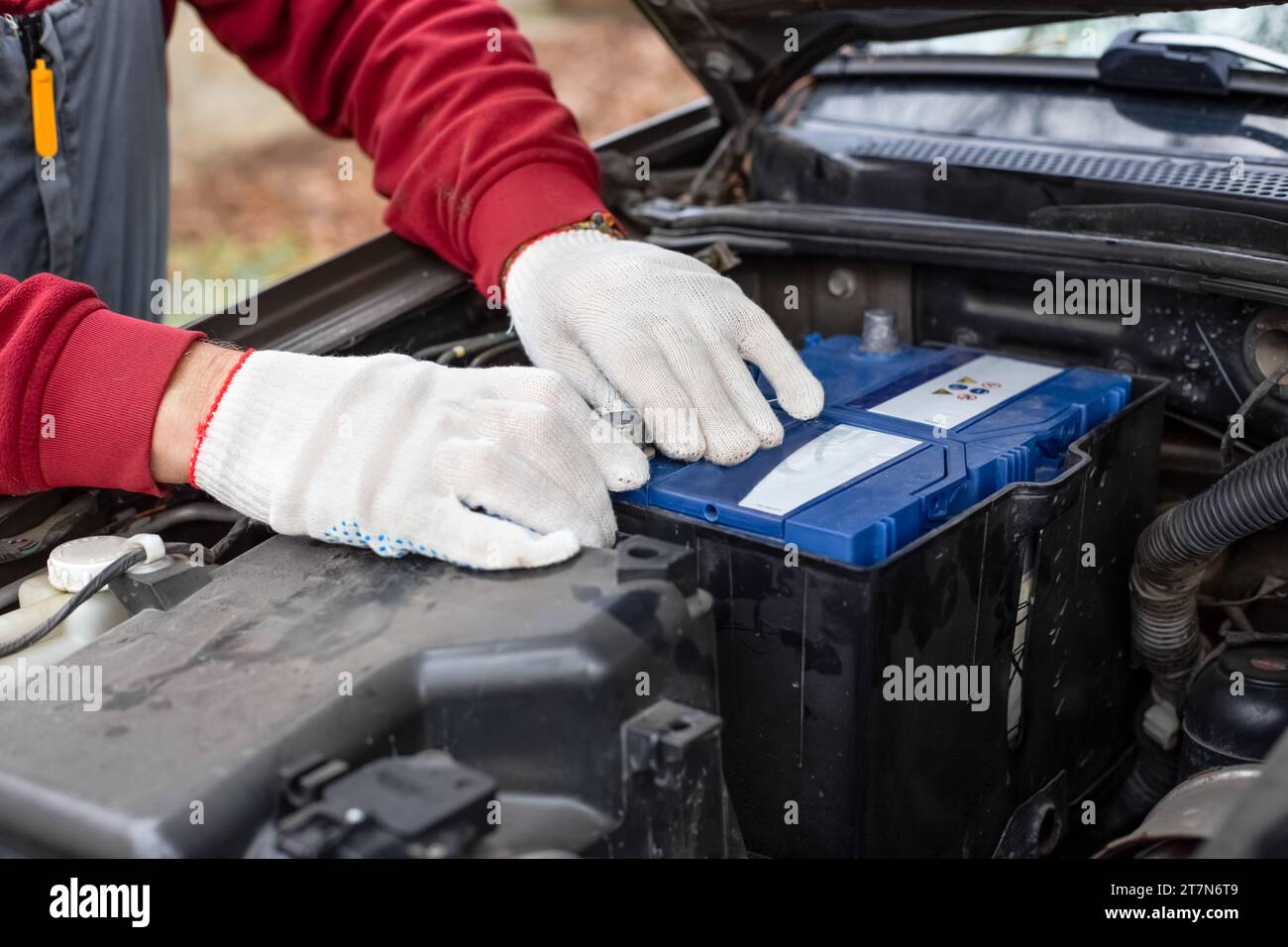 auto mechanic installs a car battery under the hood of a car. Car
