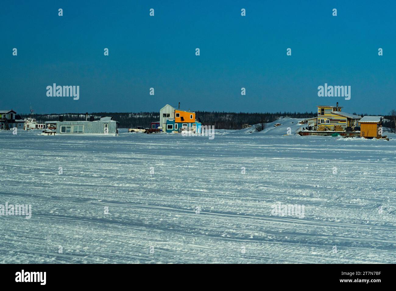 Overview of frozen Slave Lake with houseboats frozen on the ice where locals live year round accessing their homes by snowmobile or car in winter mont Stock Photo