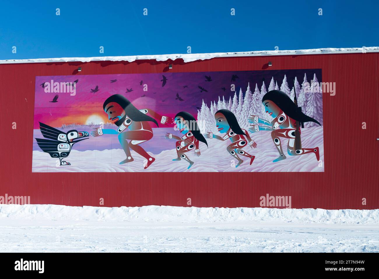 Mural on red pole barn building of native women in tribal geometric designs approaching a black raven on a winter day, Yellowknife, Northwest Territor Stock Photo