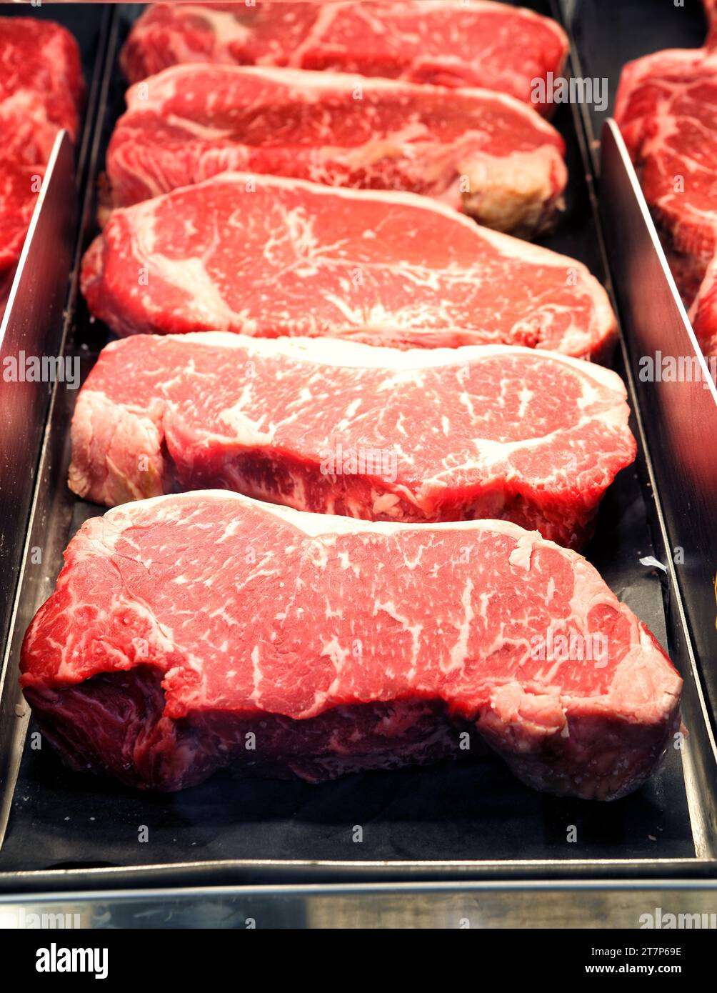A display cooler filled with fresh cut ribeye steaks for sale in a modern butcher shop. Stock Photo