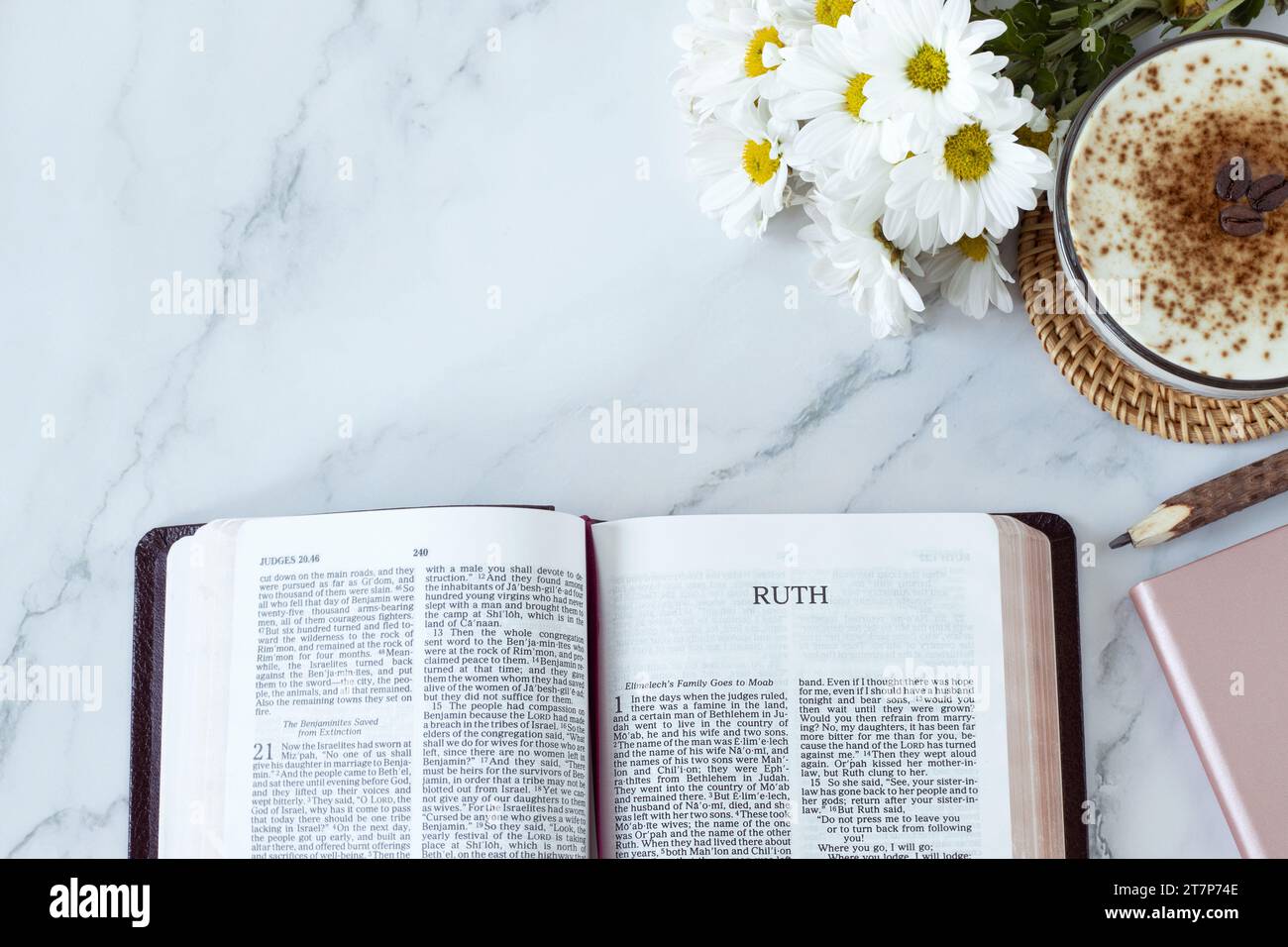 Ruth open bible book with coffee cup, flowers, pencil, and notebook on white marble background. Top table view. Copy space. Studying Old Testament. Stock Photo