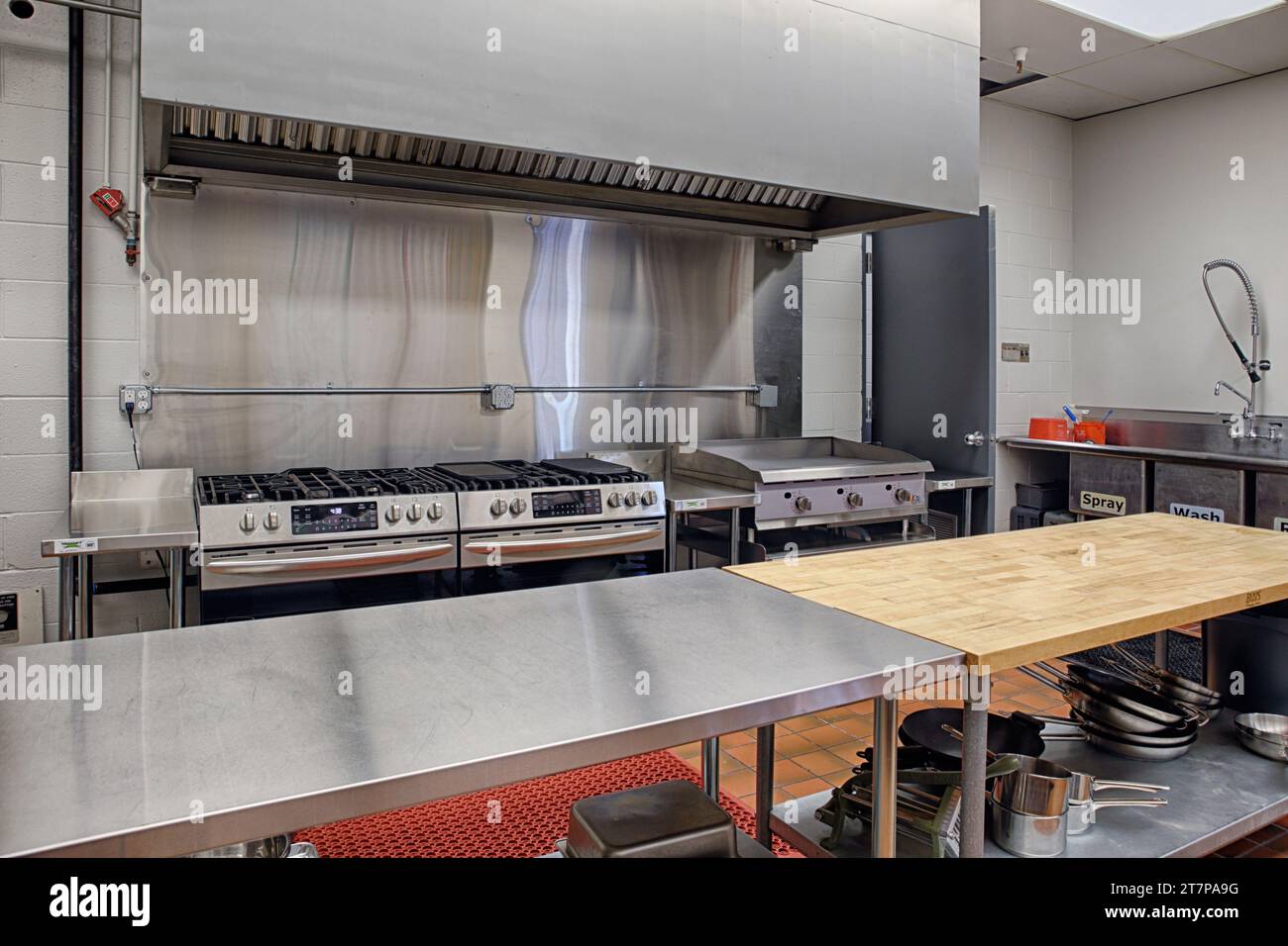 A modern stainless steel commercial kitchen, with prep area, grill, griddles, range, toasters, microwaves, and fire supression. Stock Photo