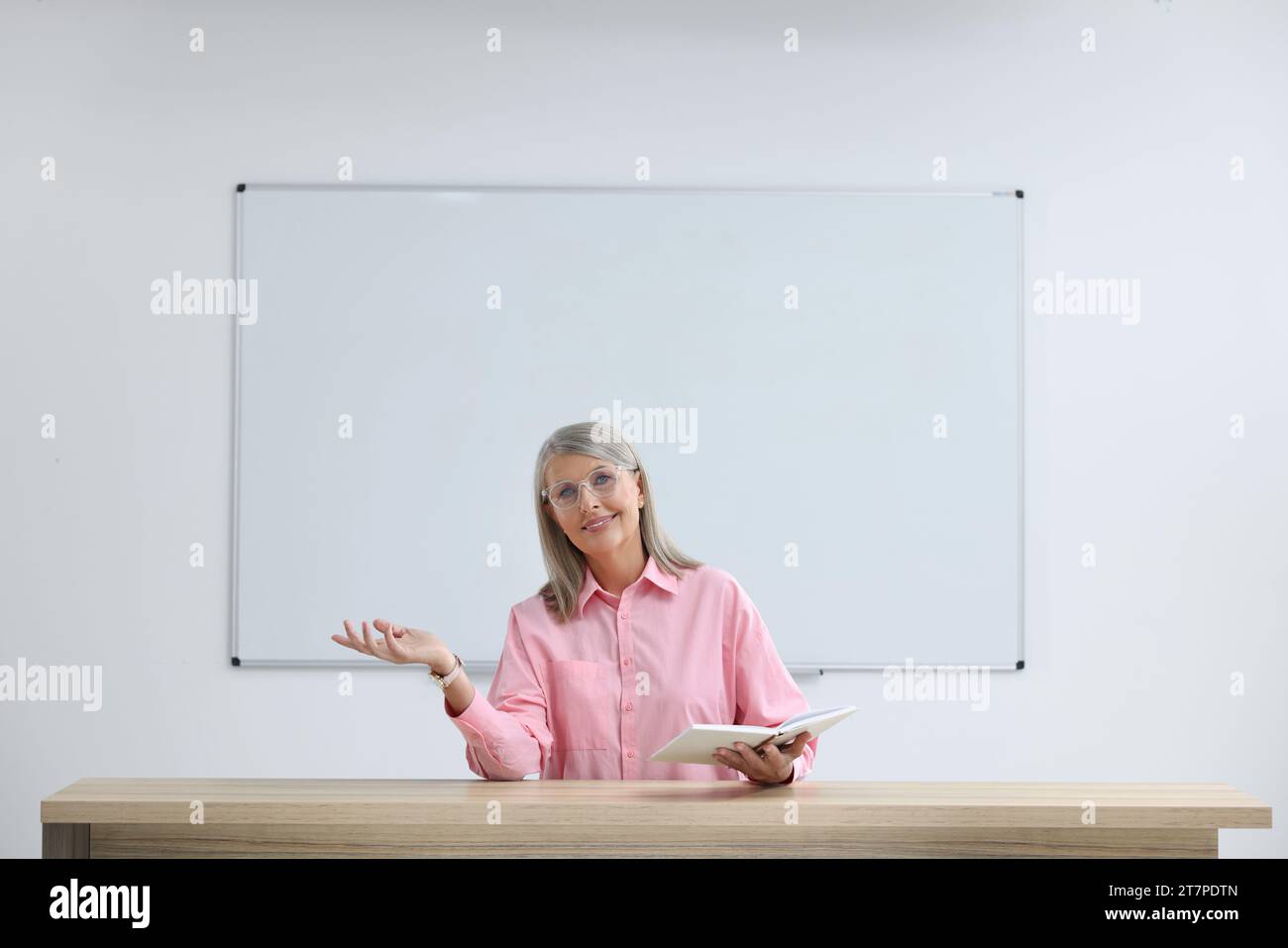 Happy professor with book giving lecture at desk in classroom Stock ...