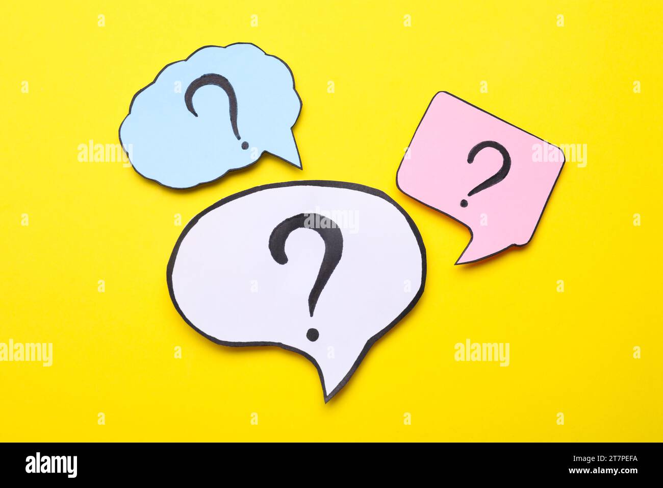 Different paper speech bubbles with question marks on yellow background, flat lay Stock Photo