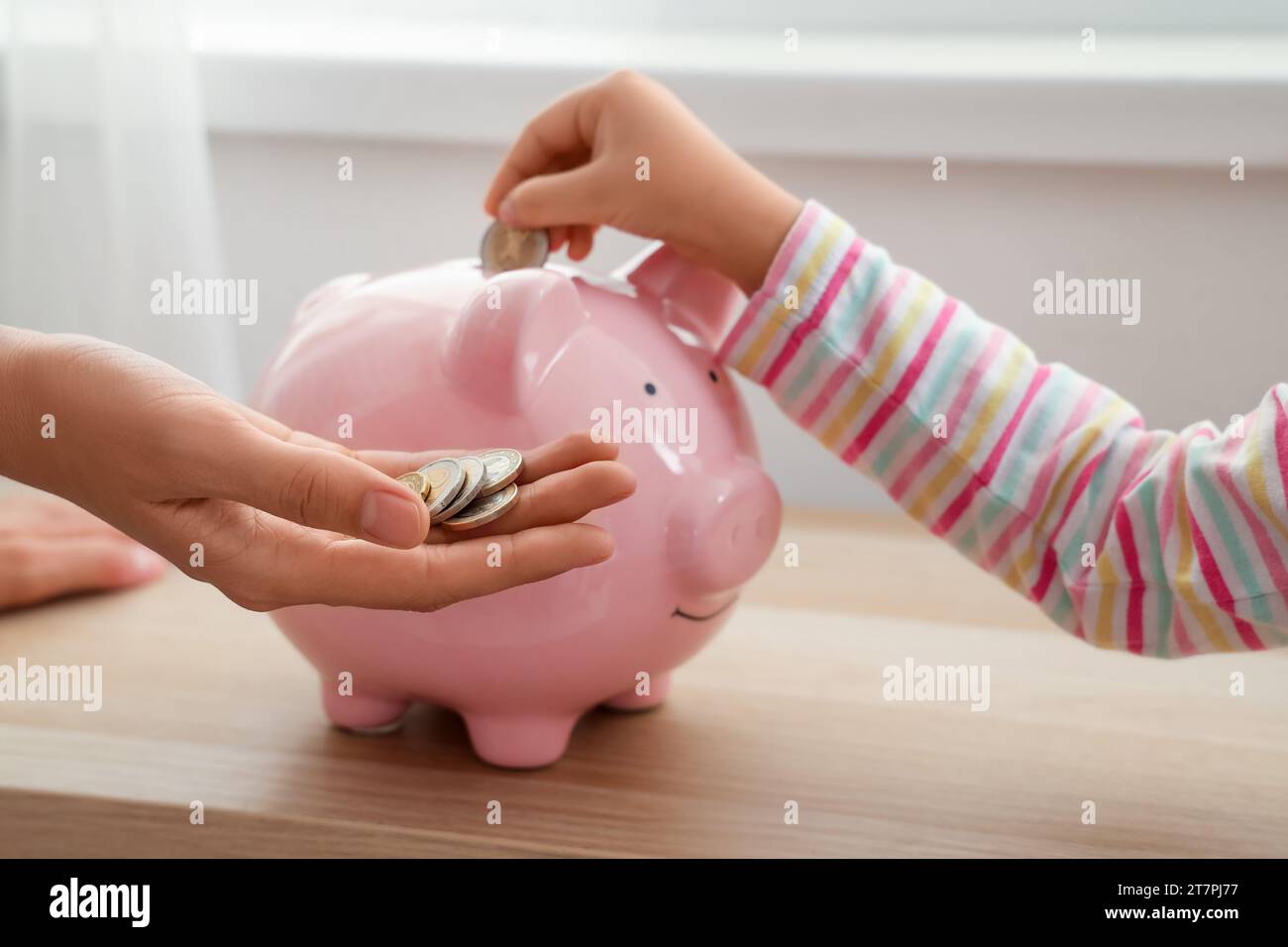Little girl with her mother putting coin into piggy bank at home ...