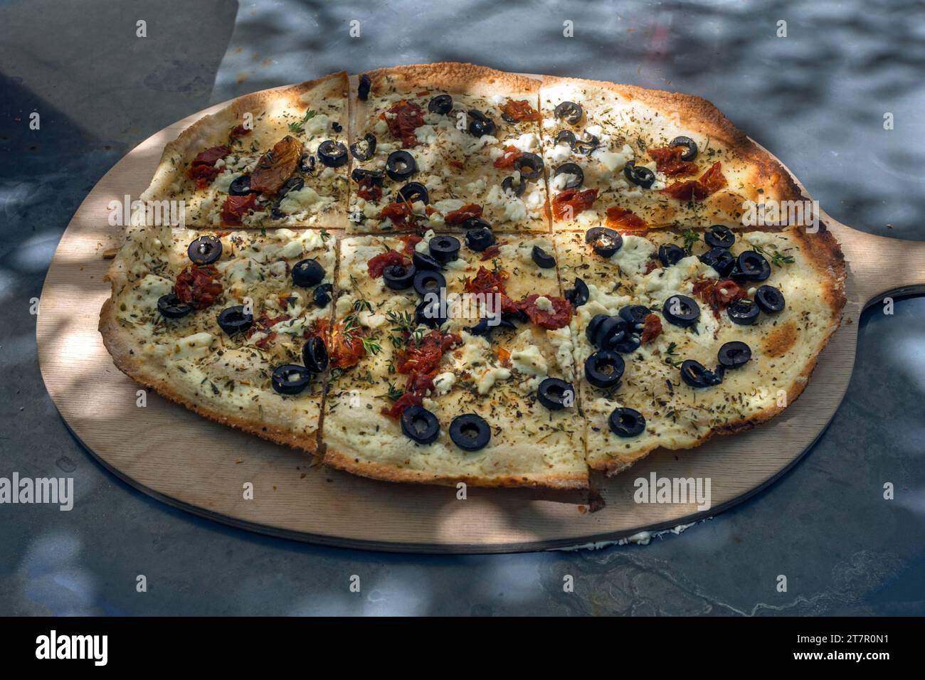 Tarte flambee with sun-dried tomatoes, feta cheese, olives and chives served on a wooden board, Bavaria, Germany Stock Photo