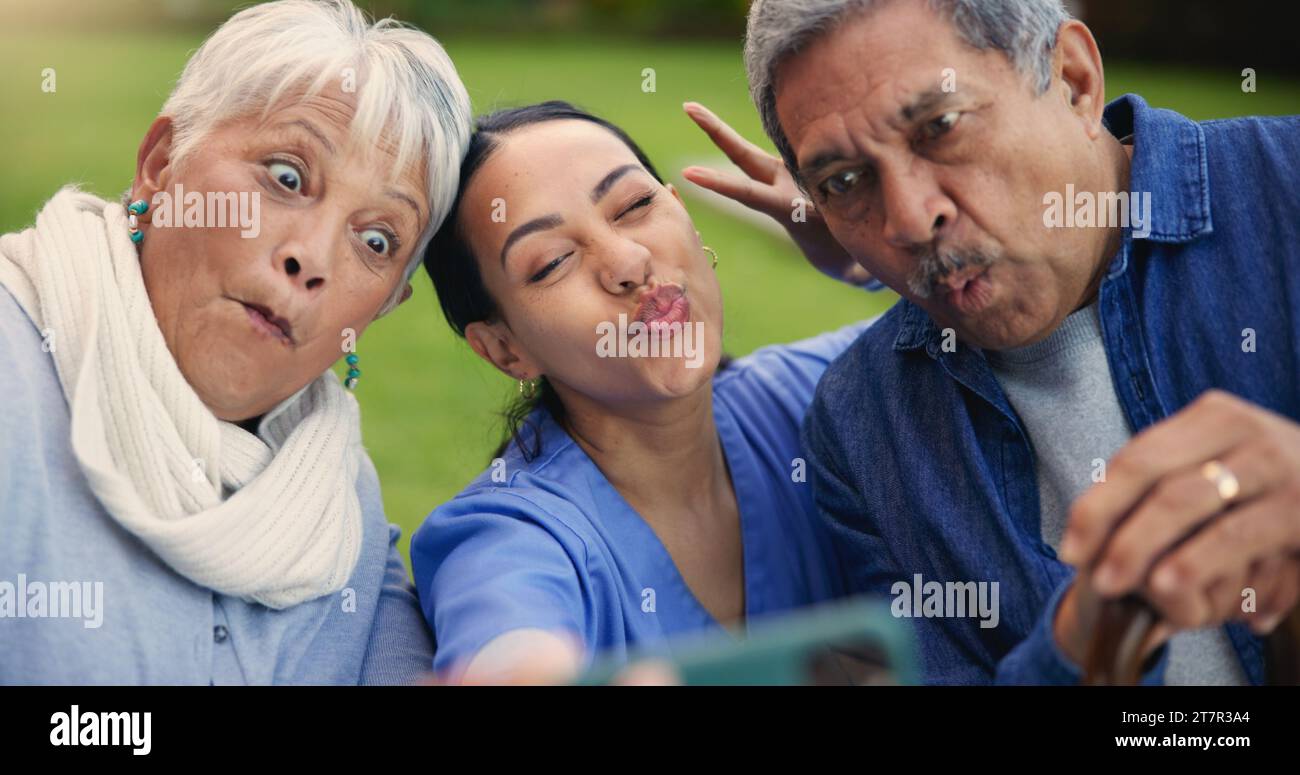 Selfie, peace sign or funny face with a nurse and old couple outdoor in an assisted living garden together. Comedy, support or wellness with a senior Stock Photo
