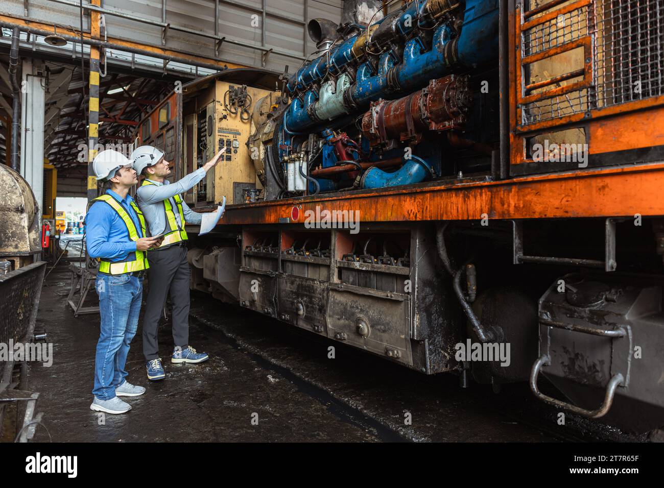 Professional engineer worker  looking at old grease oil dirty large locomotive engine plan to overhaul service. diesel train engine service. Stock Photo