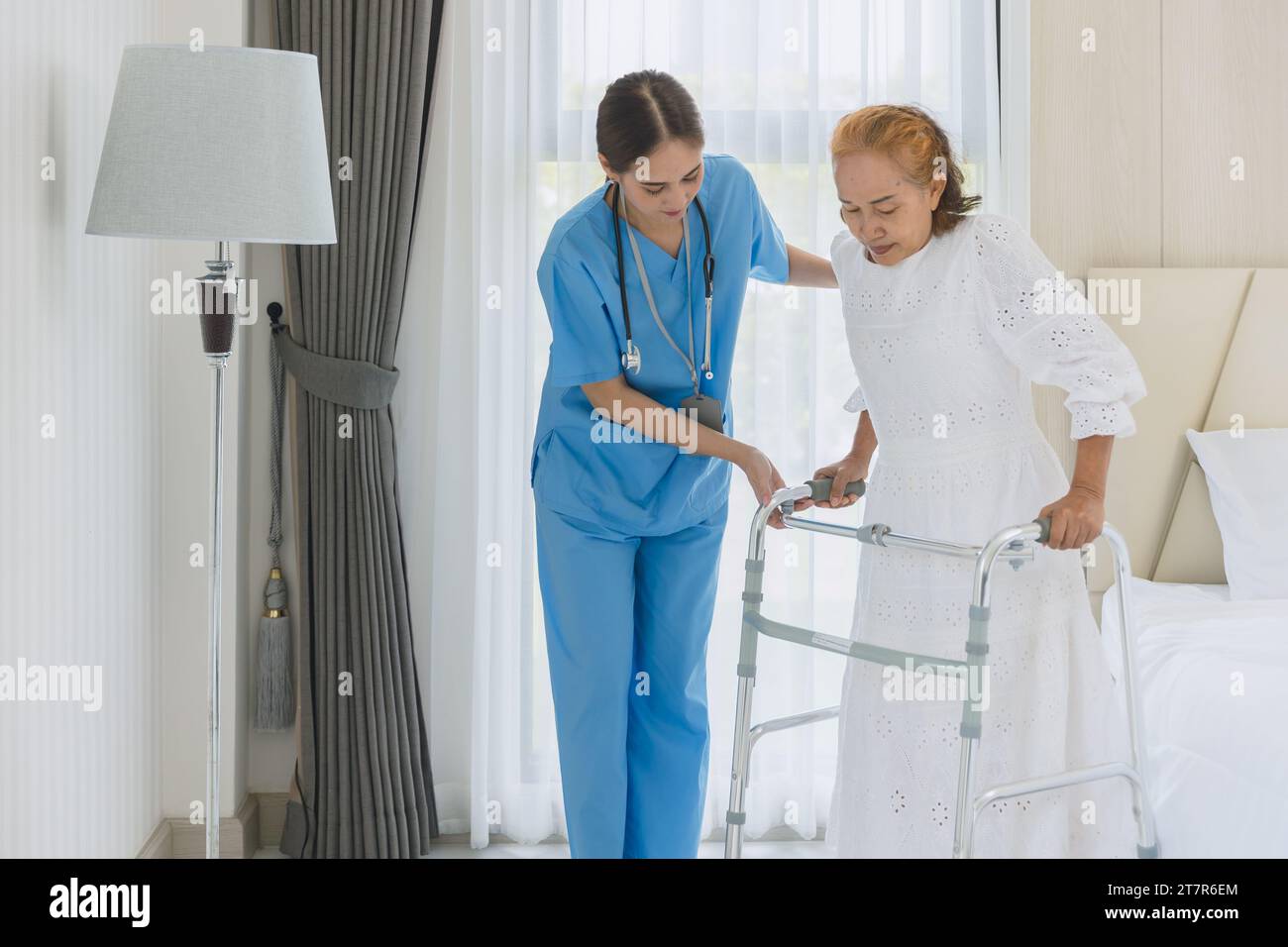Asian elderly woman practice walking using walker aid with nurse care support step walk at homecare Stock Photo