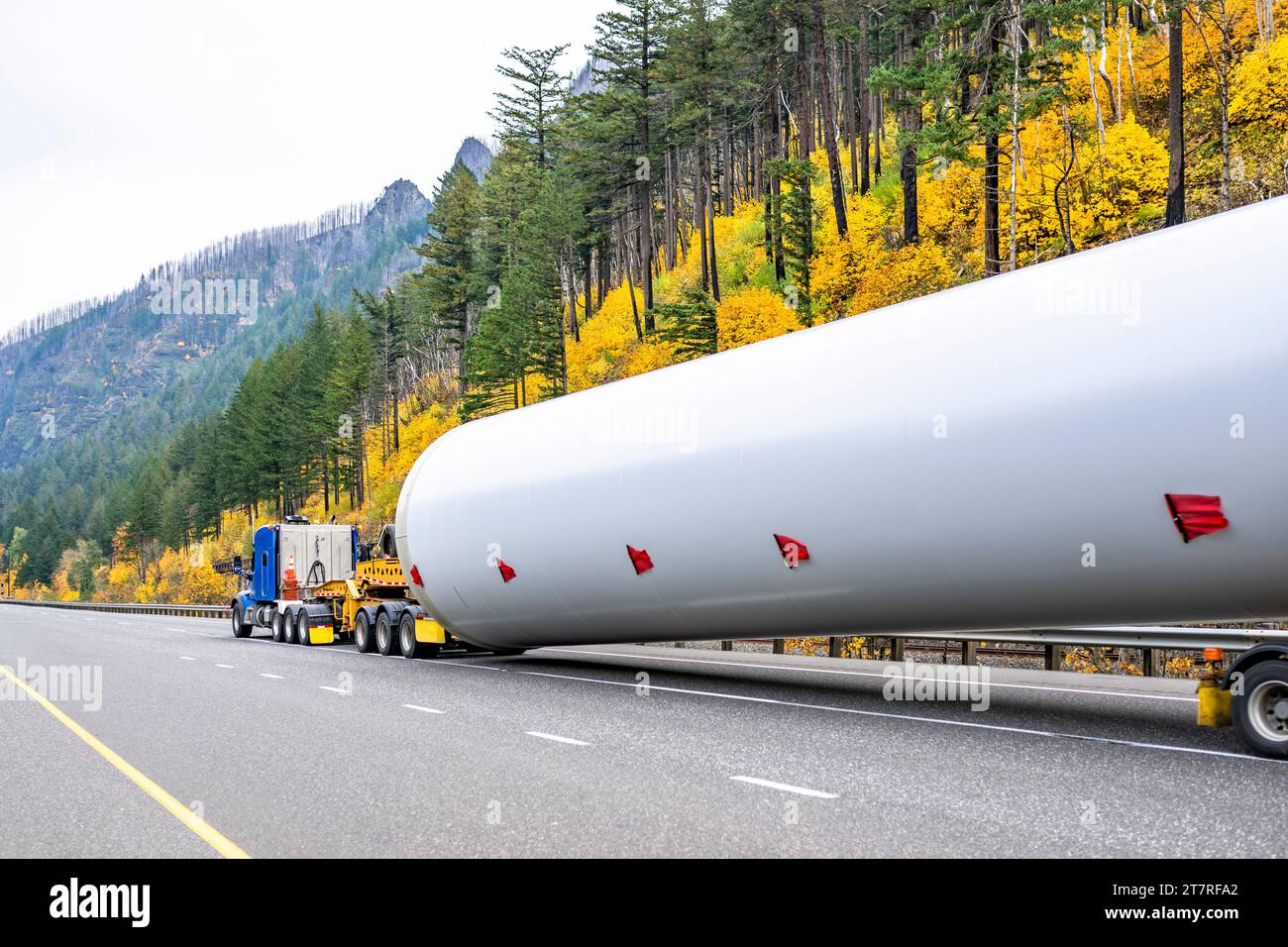 Industrial carrier big rig blue semi truck tractor with oversize load sign transporting part of oversized wind turbine pillar on semi trailer with tro Stock Photo