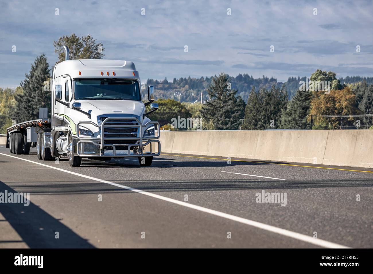 White low cab profile carrier big rig semi truck transporting flat bed