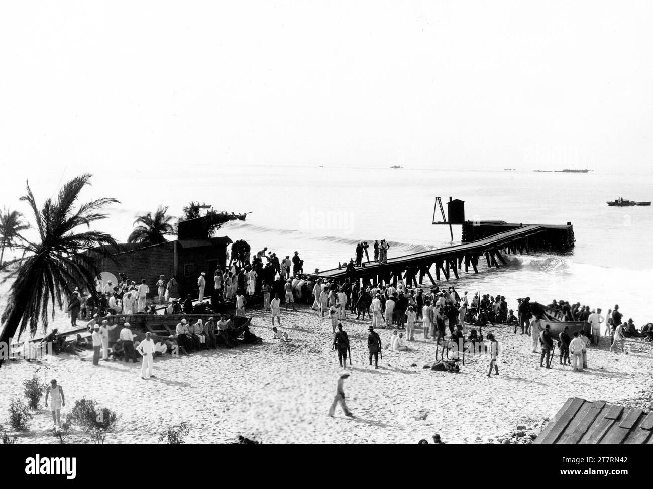 On set location candid filming the Landing at Daiquiri showing the first boatloads of Teddy Roosevelt's Rough Riders arriving on Cuban soil on set location candid at Laguna, California with Director VICTOR FLEMING standing on jetty in white shirt near movie camera during filming of THE ROUGH RIDERS 1927 director VICTOR FLEMING assistant director Henry Hathaway cinematographers James Wong Howe and E. Burton Steene associate producer B.P. Schulberg producer Lucien Hubbard Paramount Pictures Stock Photo