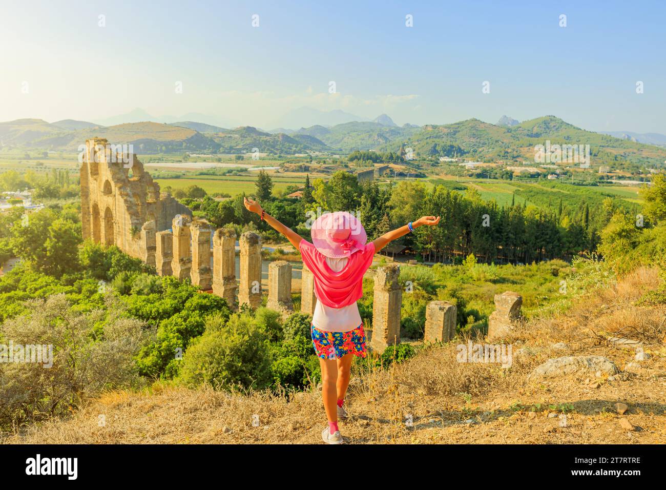 Tourist girl, enchanted by the ancient marvels of Turkey, explores the impressive Roman aqueduct of Aspendos. Against the backdrop of time-worn arches Stock Photo