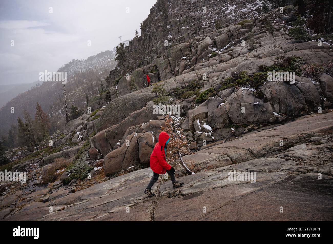 Two kids in red hike on different trails on mountainside Stock Photo
