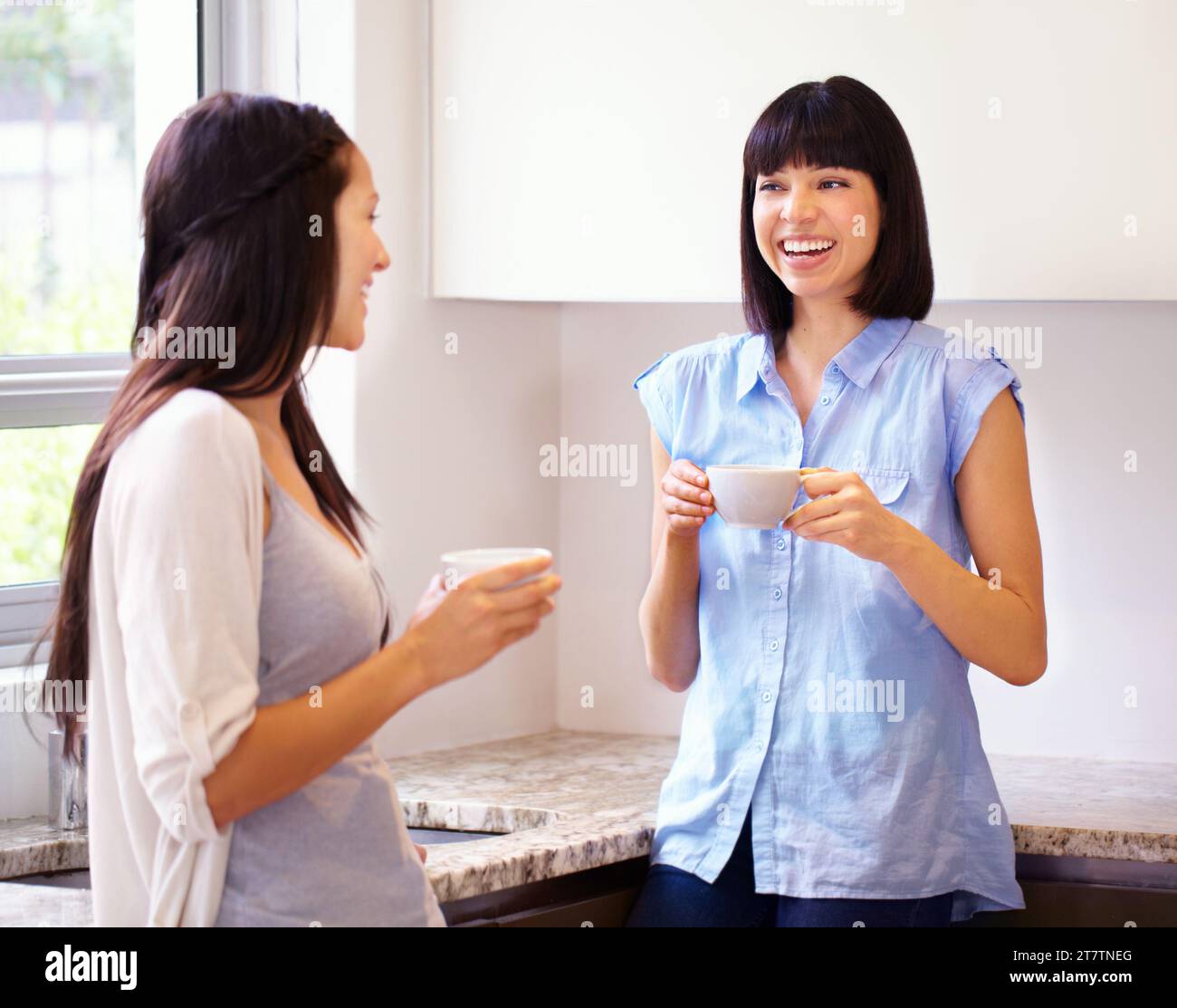Woman, friend and coffee for talk in kitchen for gossip, bonding and together. Happy people, laugh and excited emoji for discussion with hot beverage Stock Photo