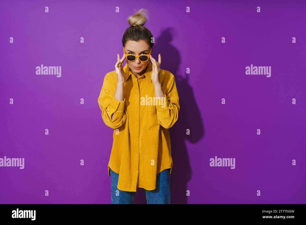 Young girl wearing yellow shirt and sunglasses making silly face expression against purple background Stock Photo