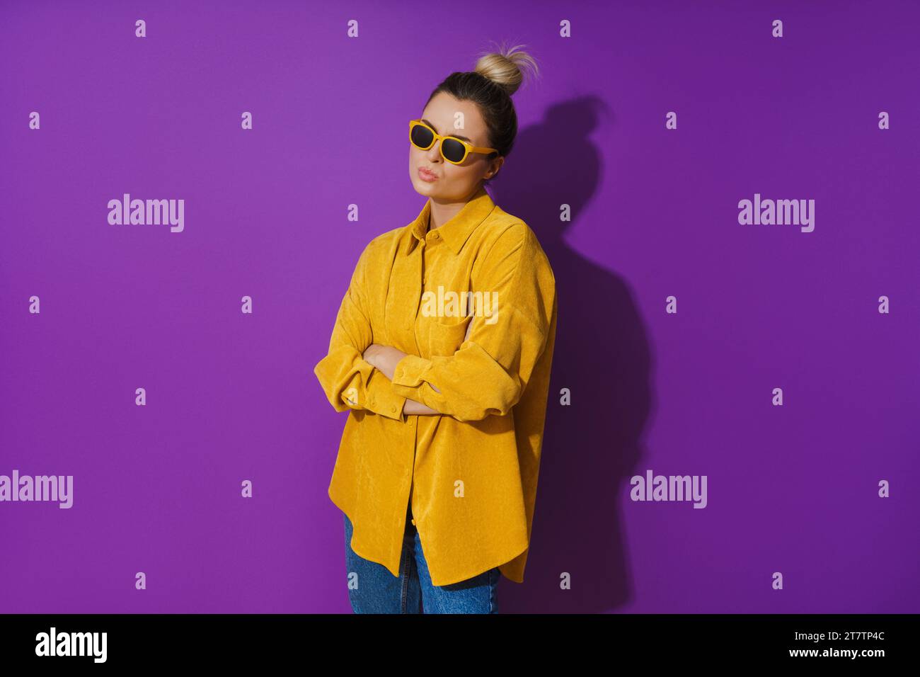 Young girl wearing yellow shirt and sunglasses showing disdain expression against purple background Stock Photo