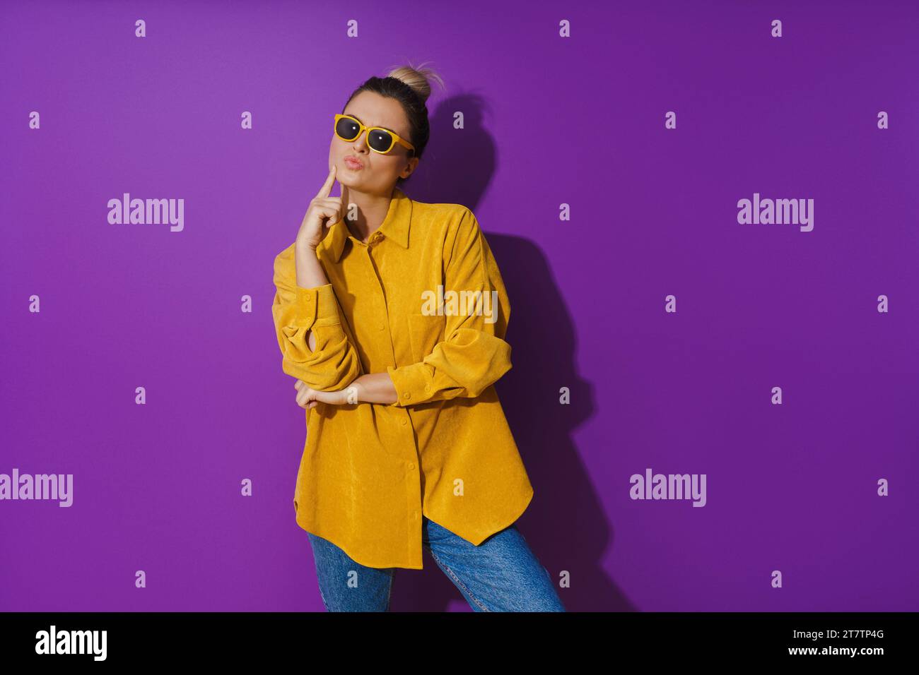 Young girl wearing yellow shirt and sunglasses showing disdain expression against purple background Stock Photo