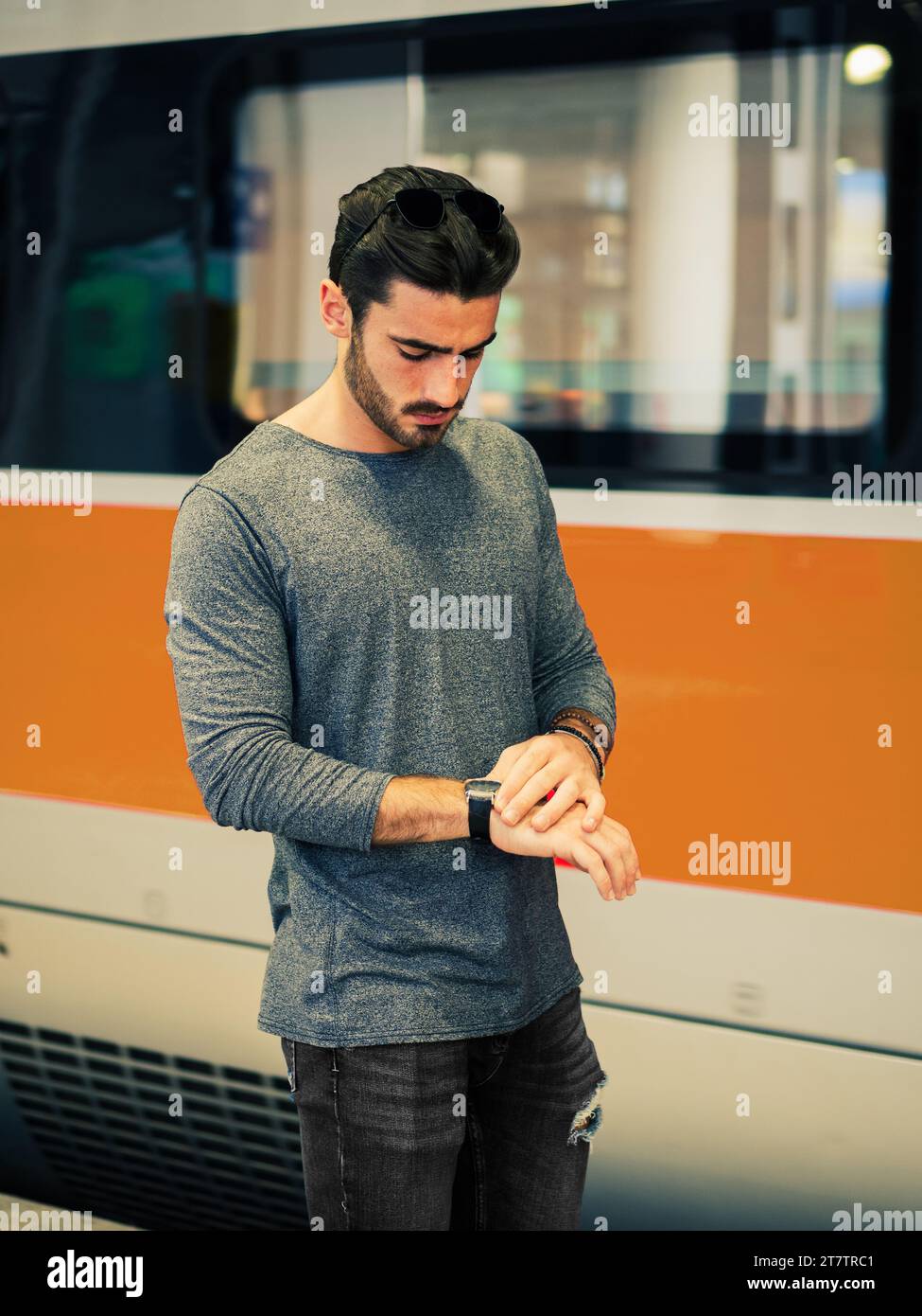 A man standing in front of a red and white train, looking at his wrist watch to check the time Stock Photo