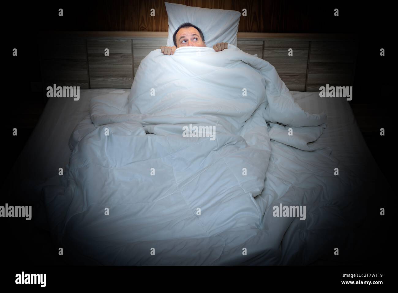 Frightened man in bed hiding under the covers Stock Photo Alamy