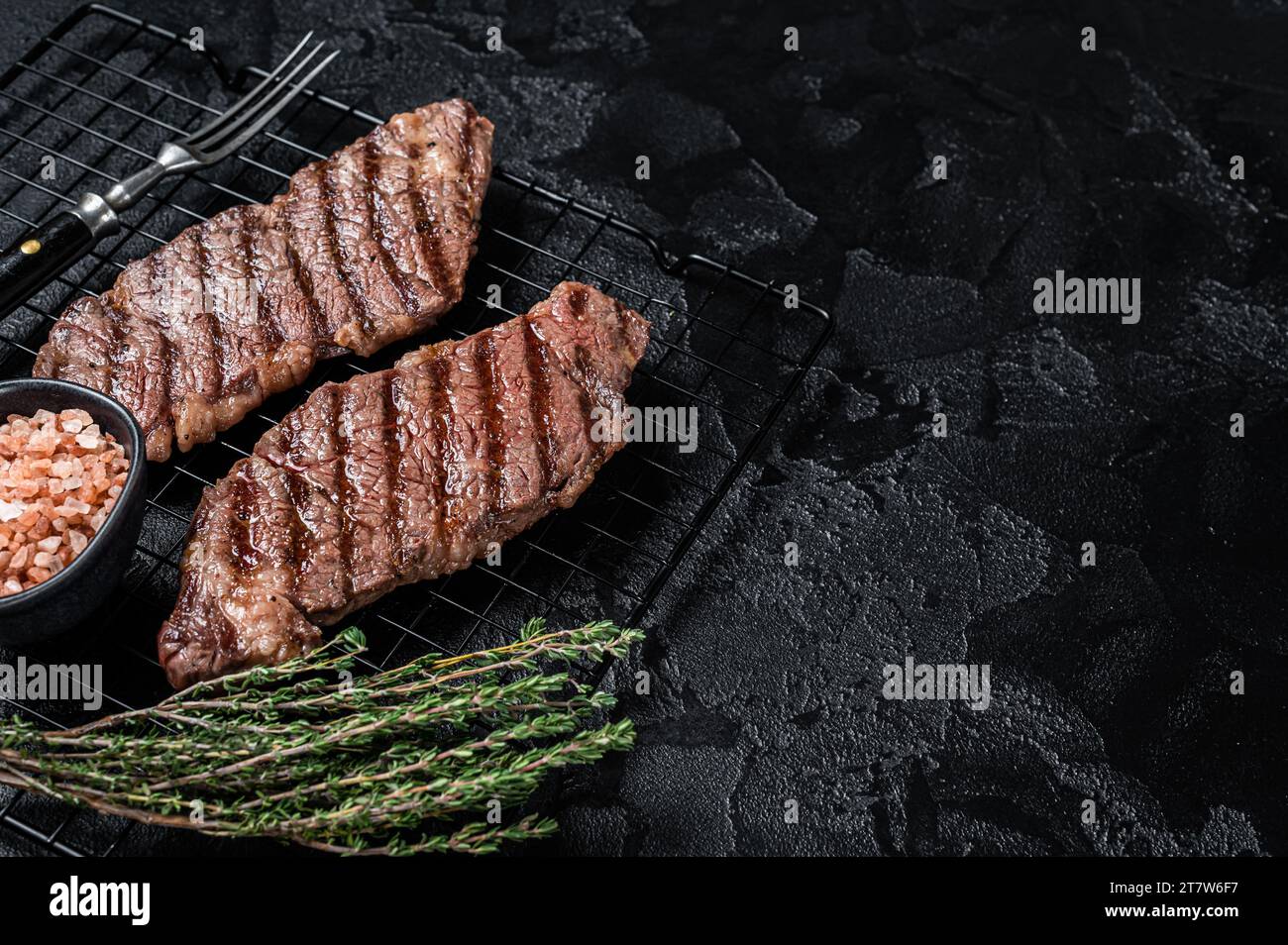 Grilled denver beef meat steak on a rack. Black background. Top view. Copy space. Stock Photo