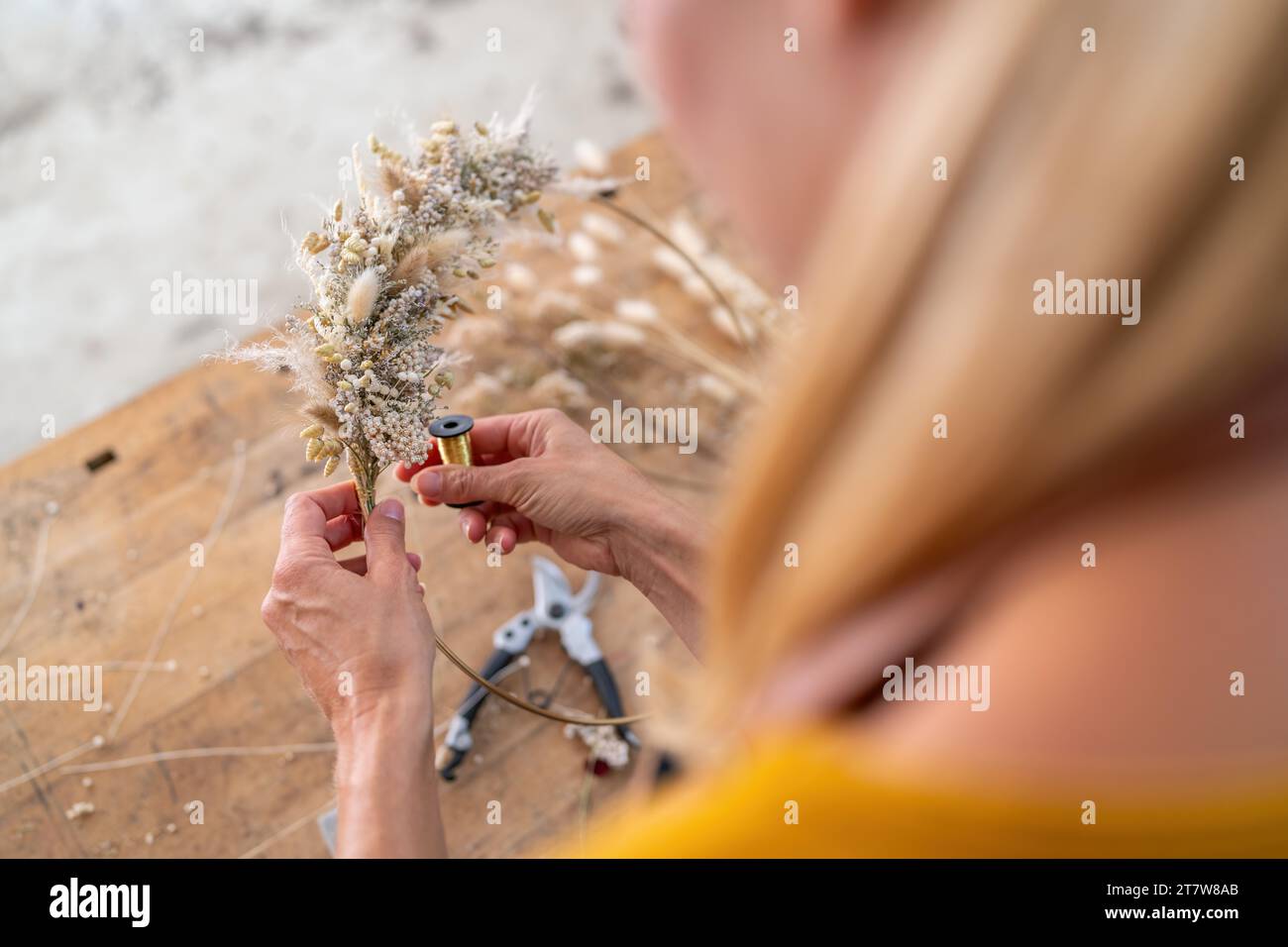 Female florist using wire to attach dried flowers to a wire hoop in a