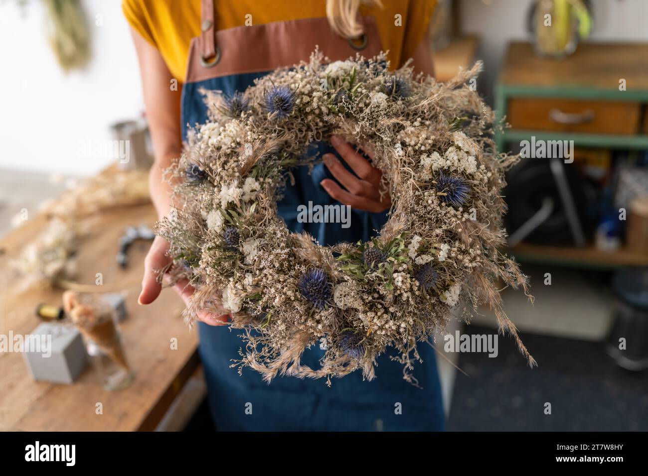 Florist presenting a nearly finished dried flower wreath, showcasing its textures and colors Stock Photo
